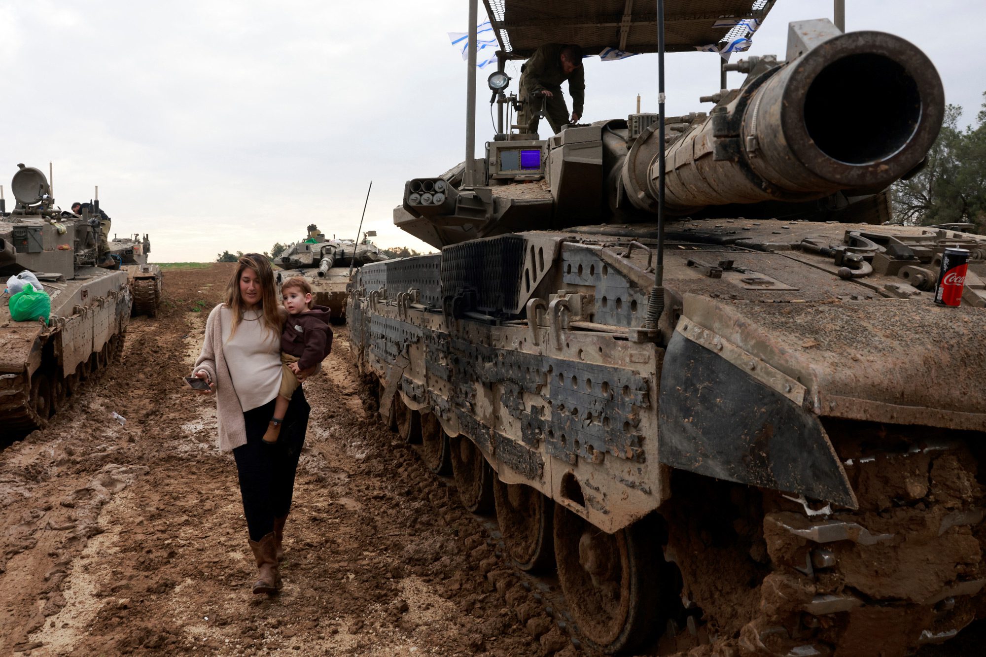 Дружина ізраїльського солдата несе свою дитину повз танк, відвідуючи чоловіка після його повернення з місії на палестинській території, 28 січня 2024 року. Фото: MENAHEM KAHANA/AFP via Getty Images